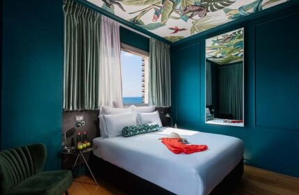 Brown Seaside Hotel room. Gay-friendly hotel with a tropical-themed ceiling, blue walls, and a view of the sea. Modern, stylish design.