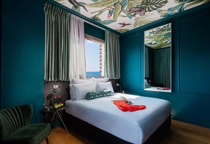 Brown Seaside Hotel room. Gay-friendly hotel with a tropical-themed ceiling, blue walls, and a view of the sea. Modern, stylish design.