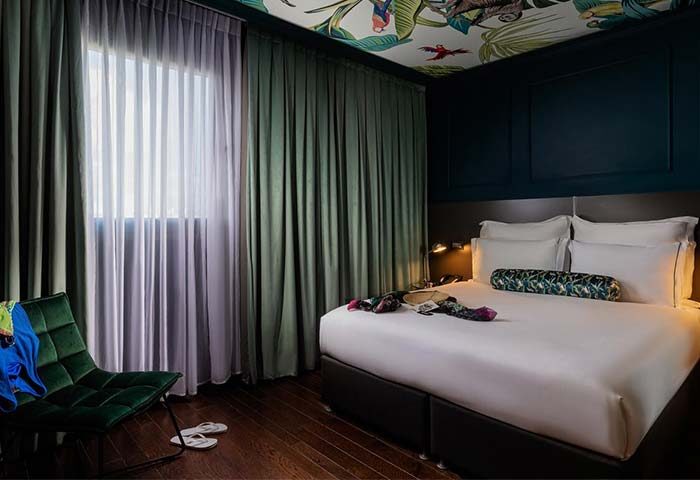 Brown Seaside Hotel bedroom interior. Gay-friendly hotel room with a bed, chair, curtains, and tropical-themed ceiling. Member of Brown Hotels.