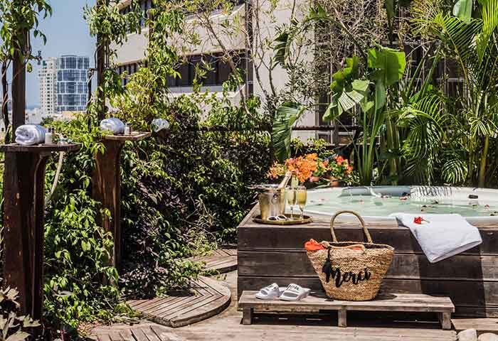 Rooftop jacuzzi at Brown TLV Hotel, a gay-friendly hotel in Tel Aviv. Champagne bucket, beach bag, and lush greenery create a relaxing vibe.