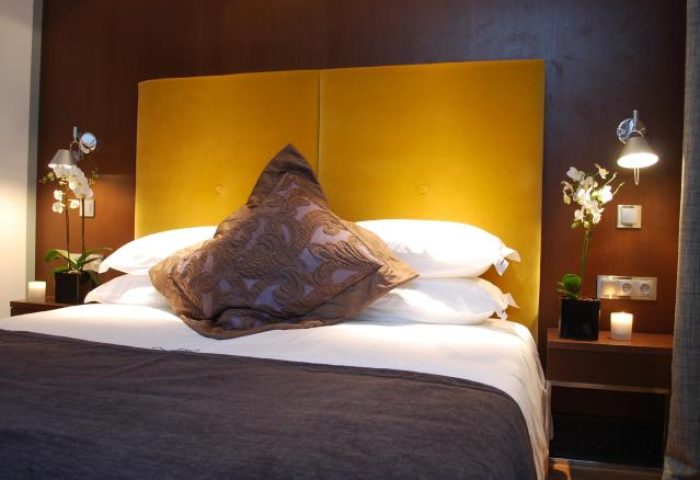 Bedroom at Browns Boutique Hotel, a gay-friendly hotel. Features a bed with a yellow headboard, brown pillow, and orchids.
