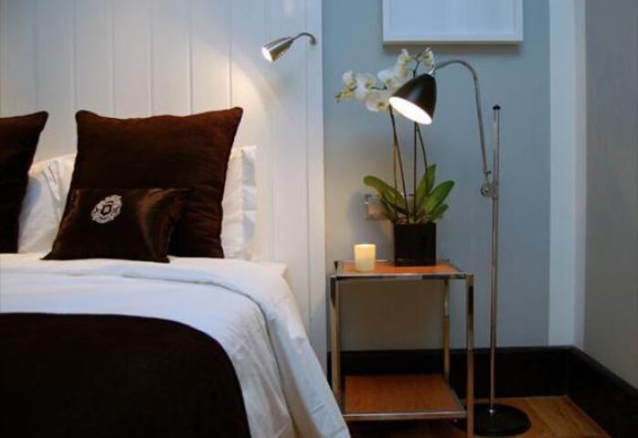 Browns Downtown Hotel room detail. Gay-friendly hotel features cozy bed with brown pillows, bedside table, lamp, orchid, and candle.