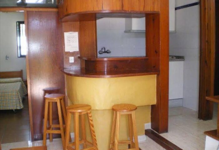 Interior view of Bungalows Tenesoya, a gay-friendly hotel. Bar with stools, kitchenette, and bedroom visible. Gay men travel.