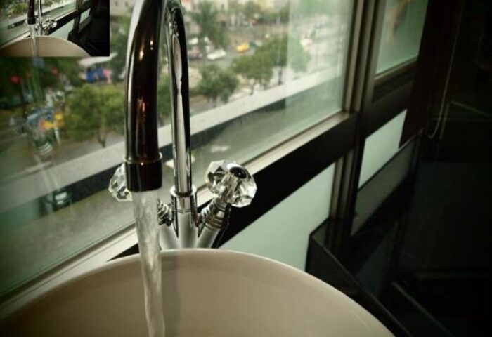 Bathroom sink and faucet at Burgary Hotel, a gay-friendly hotel. Water flows from the faucet, with a city view seen through the window.
