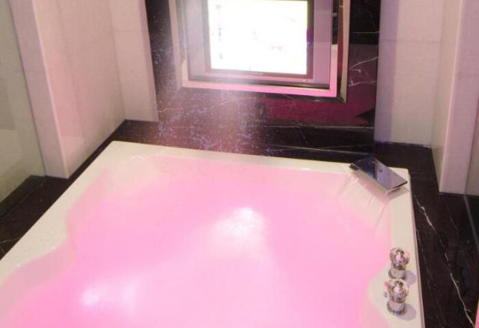 Burgary Hotel's pink-lit bathtub. A luxury gay-friendly hotel bathroom with a modern design and a built-in TV for a relaxing experience.