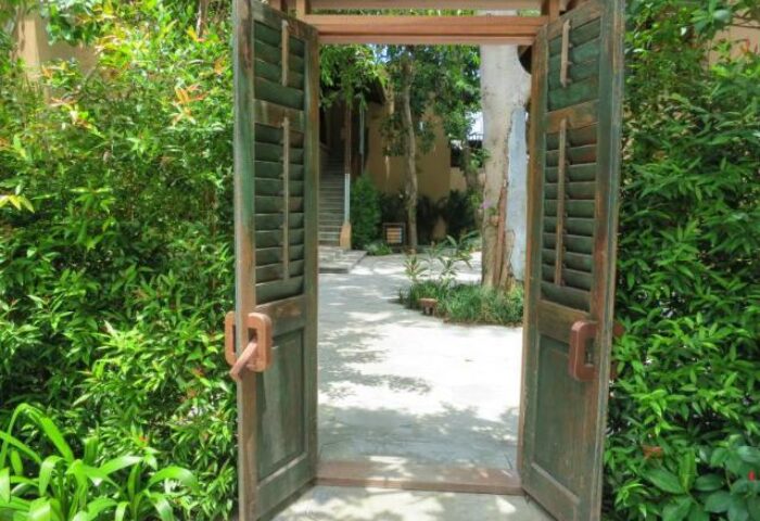 Entrance to Buri Rasa Koh Phangan, a gay-friendly hotel. Wooden doors open to a lush garden path. Ideal for gay men's travel in Thailand.
