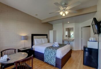 CCBC Resort Hotel room. Gay men's resort features a bed, table, TV, mini fridge, and bathroom sink. Gay-friendly hotel in Palm Springs.