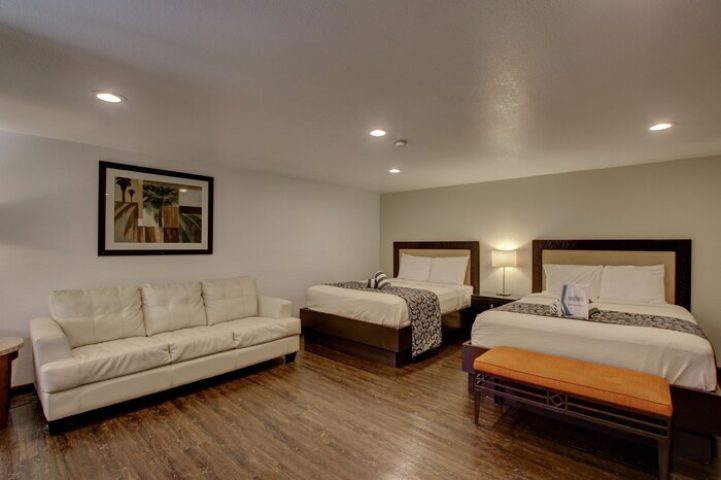 CCBC Resort Hotel room. Gay-friendly hotel with two beds, a white couch, and a bench. A gay men's resort for travel and relaxation.