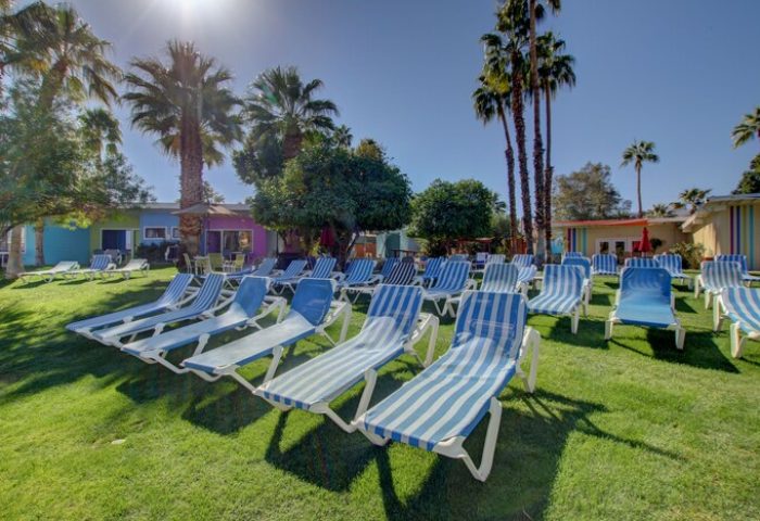 CCBC Resort Hotel, a gay men's resort. Lawn with blue striped lounge chairs, palm trees, and colorful buildings under a sunny sky.