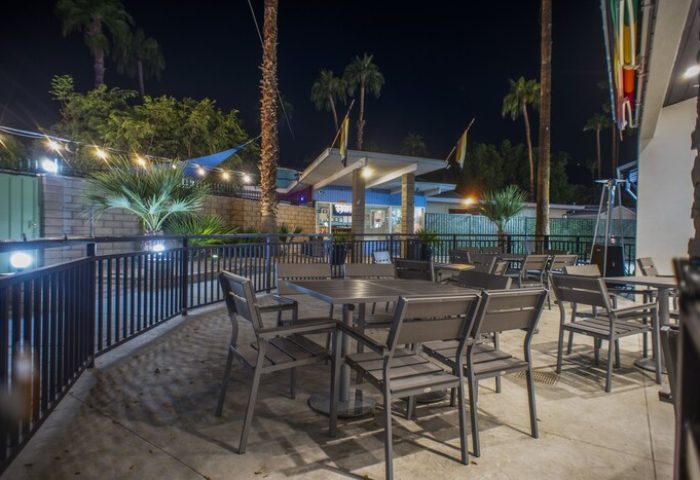 Outdoor dining area at CCBC Resort Hotel, a gay men's resort. Tables and chairs are set on a patio under palm trees at night. Gay-friendly hotel.