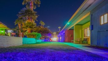 Night view of CCBC Resort Hotel, a gay men's resort. Colorful buildings, palm trees, and a starry sky create a vibrant, welcoming atmosphere.