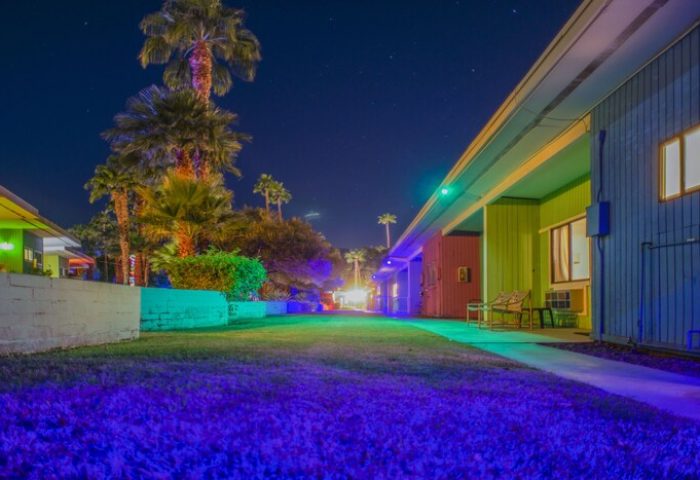 Night view of CCBC Resort Hotel, a gay men's resort. Colorful buildings, palm trees, and a starry sky create a vibrant, welcoming atmosphere.