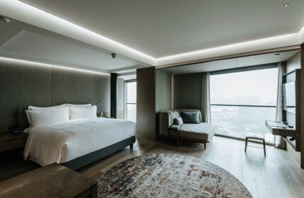 CHAO Sanlitun Beijing gay-friendly hotel room. Modern design with a king bed, chaise lounge, round rug, and city view. Perfect for gay travel.
