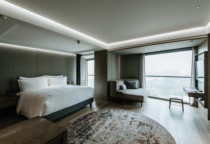 CHAO Sanlitun Beijing gay-friendly hotel room. Modern design with a king bed, chaise lounge, round rug, and city view. Perfect for gay travel.