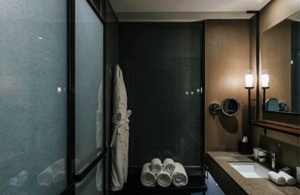 CHAO Sanlitun Beijing gay-friendly hotel bathroom. Modern design with frosted glass shower, plush towels, robe, and sleek vanity.