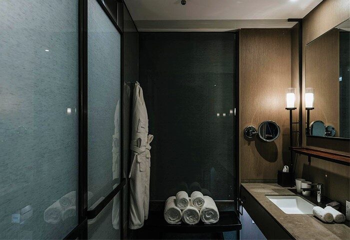 CHAO Sanlitun Beijing gay-friendly hotel bathroom. Modern design with frosted glass shower, plush towels, robe, and sleek vanity.