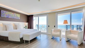 Hotel Calipolis gay-friendly room. Bedroom with bed, chairs, and balcony overlooking the sea. Gay travel in Sitges, Spain.
