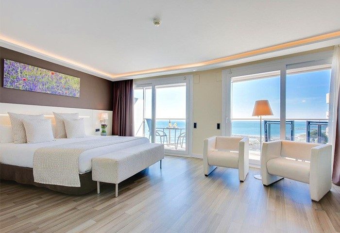 Hotel Calipolis gay-friendly room. Bedroom with bed, chairs, and balcony overlooking the sea. Gay travel in Sitges, Spain.