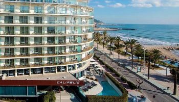 Gay-Friendly Hotel Calipolis view. Beachfront hotel with balconies overlooking the Mediterranean Sea. Palm trees line the coast. Gay travel.