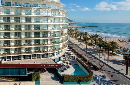 Gay-Friendly Hotel Calipolis view. Beachfront hotel with balconies overlooking the Mediterranean Sea. Palm trees line the coast. Gay travel.
