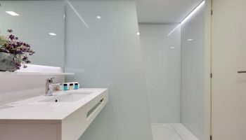Hotel Calipolis bathroom. Modern, bright interior with white sink, shower, and frosted glass. Gay-friendly hotel design for travel advice.
