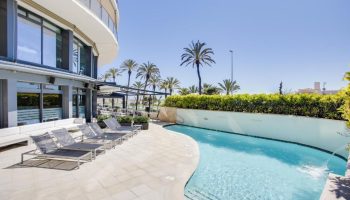 Hotel Calipolis pool area, a gay-friendly hotel. Loungers, palm trees, and blue sky. Ideal for gay men's travel.