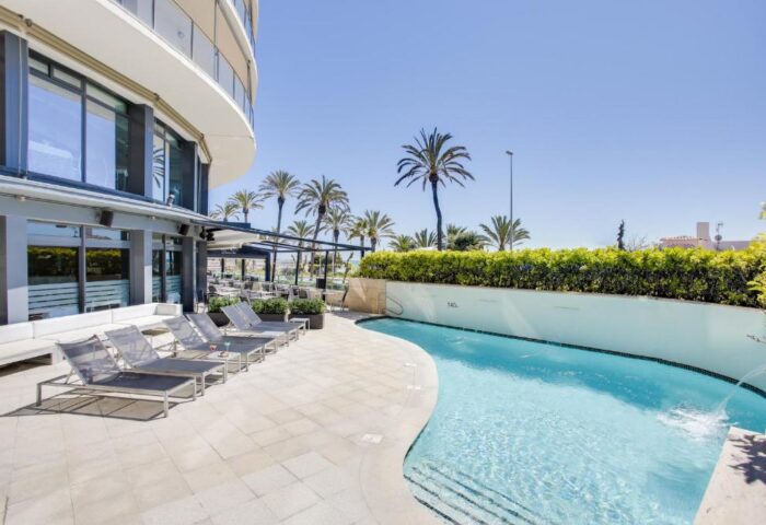 Hotel Calipolis pool area, a gay-friendly hotel. Loungers, palm trees, and blue sky. Ideal for gay men's travel.