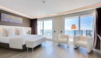 Hotel Calipolis gay-friendly room. Bright bedroom with sea view, balcony, white chairs, and a comfortable bed. Perfect for gay travel in Sitges.