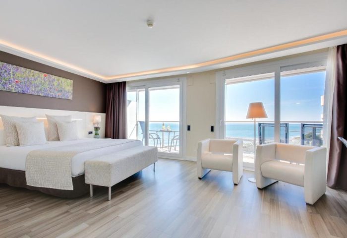 Hotel Calipolis gay-friendly room. Bright bedroom with sea view, balcony, white chairs, and a comfortable bed. Perfect for gay travel in Sitges.