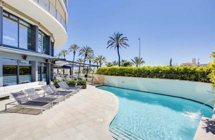 Hotel Calipolis gay-friendly pool area. Loungers by the pool in Sitges, Spain. Palm trees and blue sky. Gay travel destination.