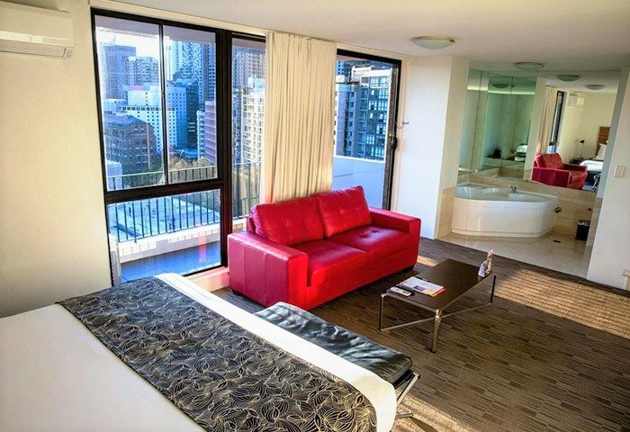 Cambridge Hotel gay-friendly room. Interior view features a red sofa, bed, city skyline, and bathroom with a tub. Modern hotel design.