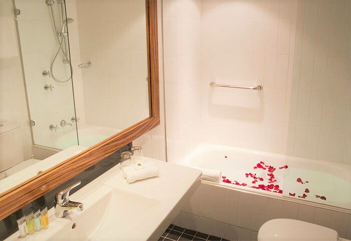 Bathroom at Cambridge Hotel, a gay-friendly hotel. Bathtub with rose petals, sink, mirror, and shower. Ideal for romantic gay travel.