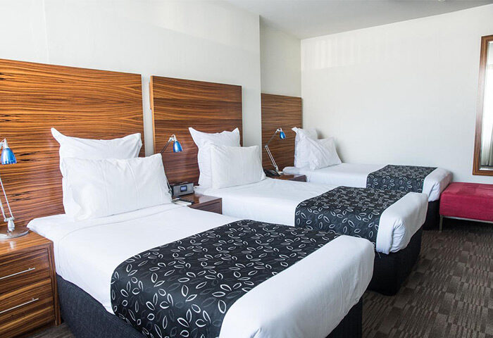 Cambridge Hotel triple room. Gay-friendly hotel with three beds, wooden headboards, bedside tables, and lamps. Ideal for gay travel groups.