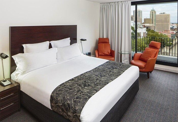 Cambridge Hotel room view. Gay-friendly hotel with a king-size bed, city view, and two orange chairs. Ideal for gay men travel.