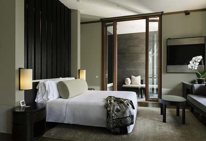 Capella Singapore Hotel room. Gay-friendly hotel featuring a bed with a decorative throw and a balcony with seating. Luxury travel.