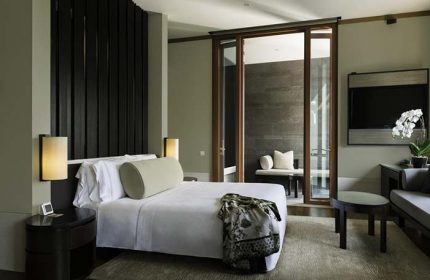 Capella Singapore Hotel room. Gay-friendly hotel featuring a bed with a decorative throw and a balcony with seating. Luxury travel.
