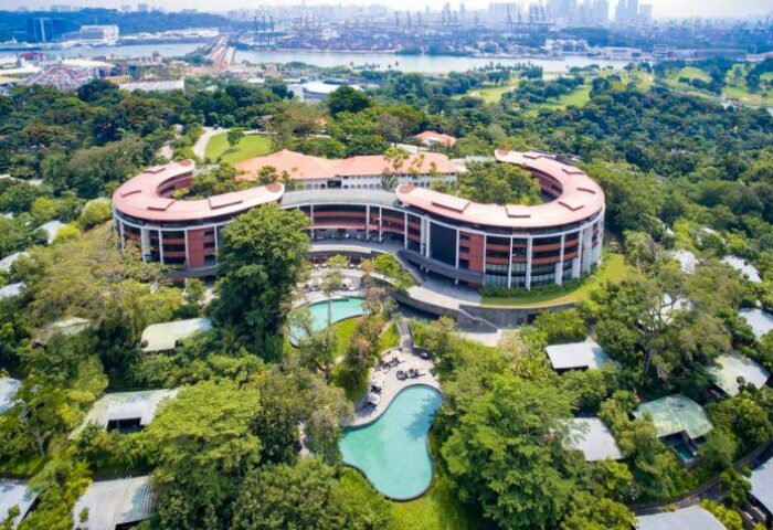 Capella Singapore Hotel aerial view. Gay-friendly hotel with pools, surrounded by lush greenery. Luxury travel destination.