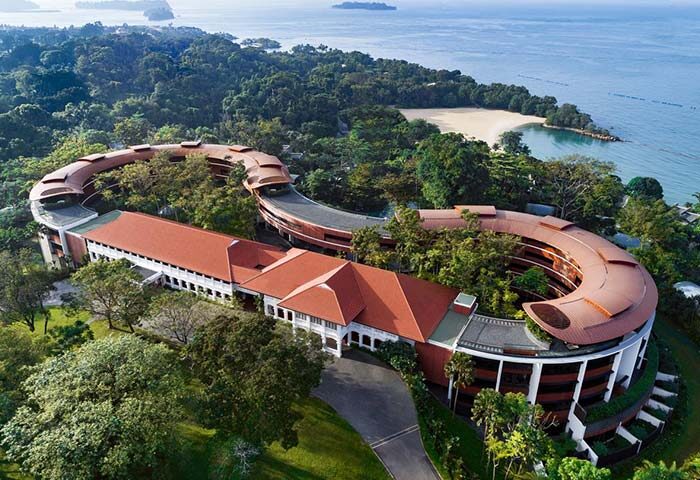 Aerial view of Capella Singapore Hotel, a gay-friendly resort with unique architecture, nestled in lush greenery near the beach. Perfect for gay travel.