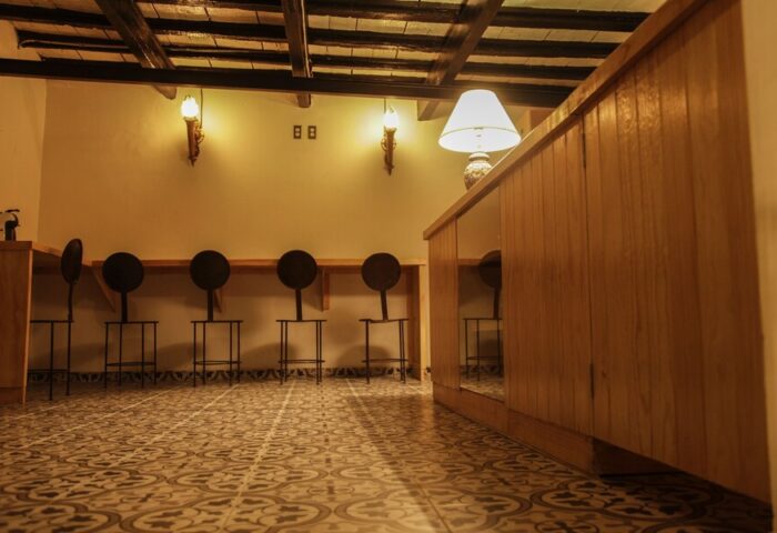 Interior of a Gay-Friendly Capsule Hostel. Features a tiled floor, wooden counter, and unique round-backed stools. Warm lighting creates a cozy vibe.