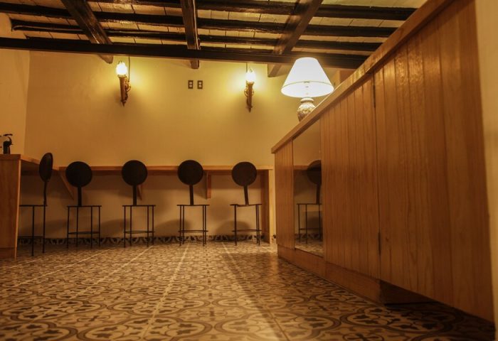 Interior of a Gay-Friendly Capsule Hostel. Features a tiled floor, wooden counter, and unique round-backed stools. Warm lighting creates a cozy vibe.