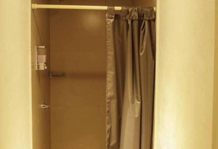 Shower stall in a capsule hostel. Gray curtain, dispenser, & shower head. Gay-friendly hotel bathroom. Budget travel for gay men.