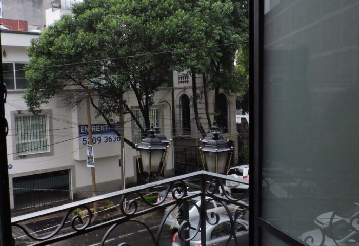 View from a gay-friendly capsule hostel balcony. Street scene with cars, trees, and buildings. Travel lodging for gay men.