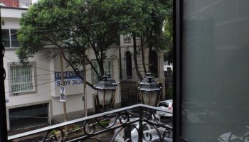 View from a gay-friendly capsule hostel balcony. Street scene with cars, trees, and buildings. Travel lodging for gay men.
