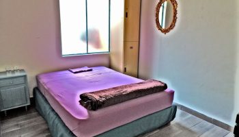 Capsule Hostel room: bed with purple sheets, brown blanket, lockers, and mirror. Gay-friendly hotel for gay men travel advice.