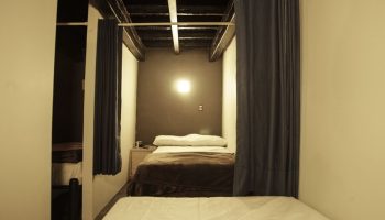 Interior of a gay-friendly capsule hostel. Sleeping pod with bed, curtain, and bedside table. Budget-friendly travel accommodation.