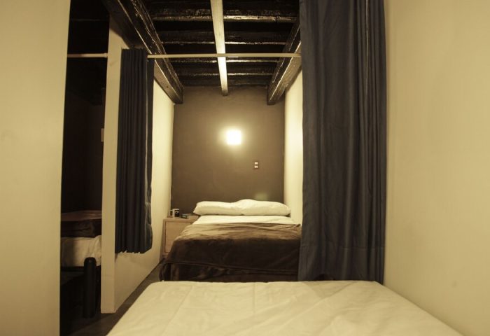 Interior of a gay-friendly capsule hostel. Sleeping pod with bed, curtain, and bedside table. Budget-friendly travel accommodation.