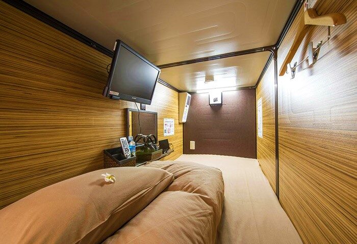 Interior of Anshin Oyado Premier Tokyo Shinjuku Station capsule hotel, a gay-friendly option. Bed, TV, and amenities in a compact space.