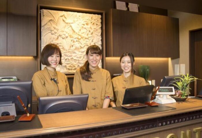 Anshin Oyado Premier Tokyo Shinjuku Station's reception desk. Three smiling women in uniforms. Gay-friendly capsule hotel in Shinjuku, Japan.