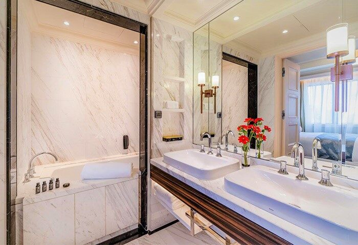 Caravelle Saigon Hotel's luxurious bathroom. Marble, double sinks, tub, and red flowers. A gay-friendly hotel for discerning travelers.