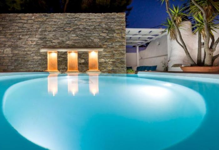 Carbonaki Hotel's pool at night. Gay-friendly hotel with lit wall alcoves reflecting in the water. Serene Mykonos travel for gay men.